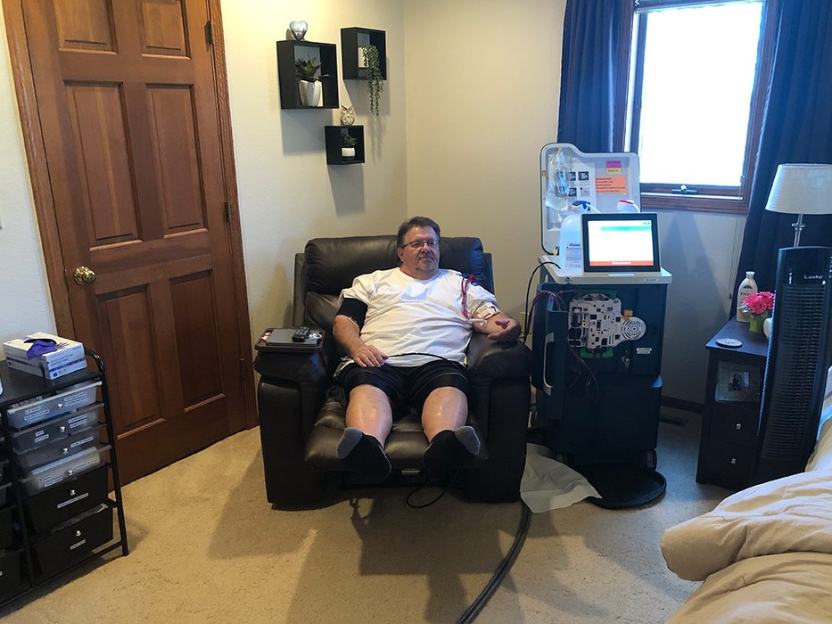 A patient comfortably completing a home hemodialysis treatment in her living room while a family member sits nearby